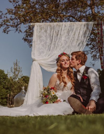 Focení svatebního editoriálu v Pouzdřanech u Brna na Ambrožově dvoře, kde sedí nevěsta a ženich před slavobránou a užívají si sluníčka.